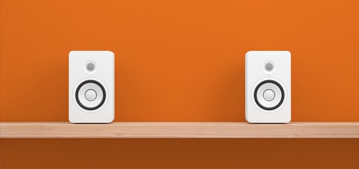 Two audio speakers sitting on a shelf in front of an orange wall